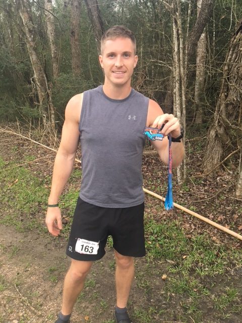 Male athlete holding medal for running 50 mile trail race