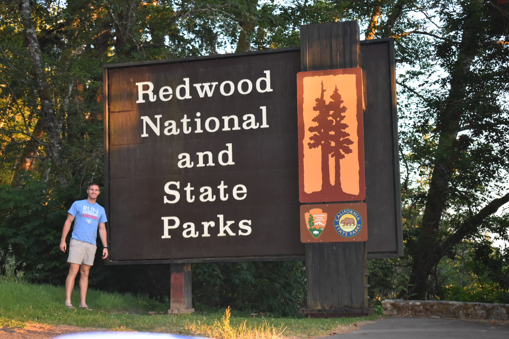 guy standing in front of redwood national park entrance sign