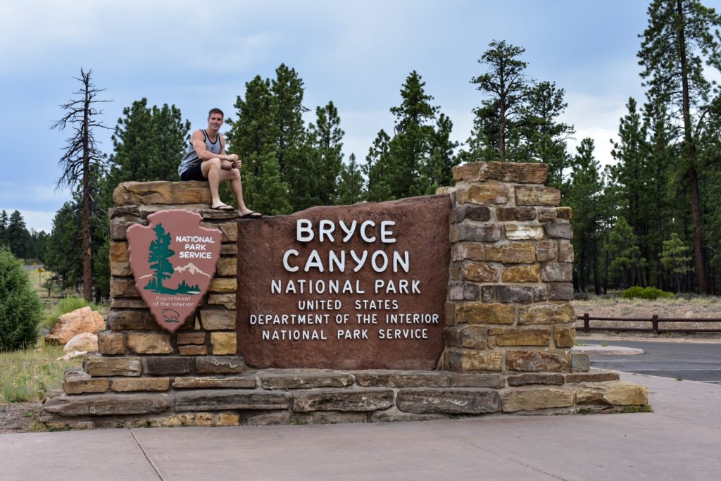 Guy sitting on top of entrance sign to Bryce Canyon national park