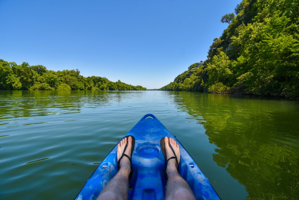 view from sitting in a blue kayak looking down the middle of a calm river