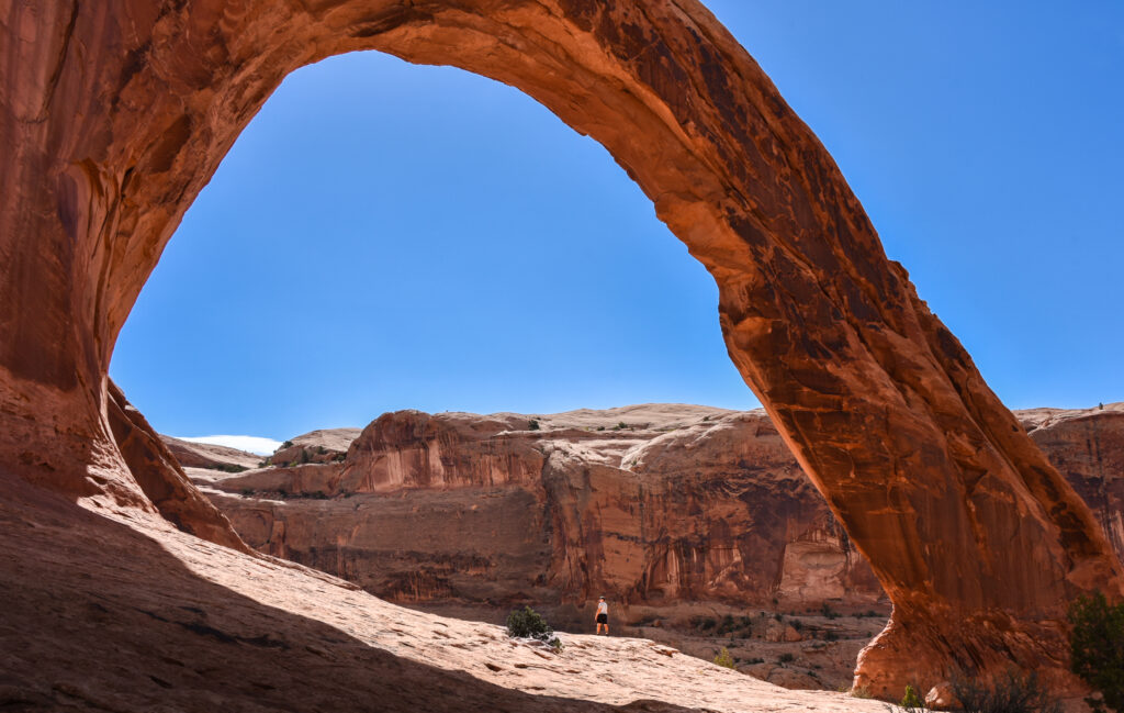 Man standing under large sandstone arch in utah